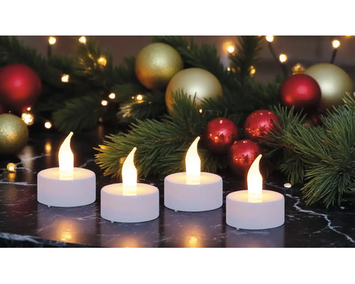 Vier weiße LED-Teelichter mit warm leuchtenden Flammen auf einer dunklen Marmoroberfläche, festliche Weihnachtsdekoration im Hintergrund.