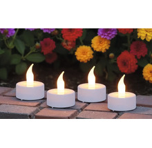 Vier LED-Teelichter mit warmem Licht auf Steinplatten vor bunten Blumen im Garten.