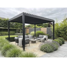 Pergola bioclimatique moderne en aluminium au-dessus d'un salon de jardin gris sur une terrasse en pierre, entourée de verdure.