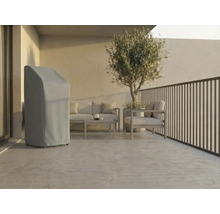 Terrasse moderne et lumineuse avec une housse de protection grise pour matériel de jardin, des meubles de salon en métal et un olivier en pot.