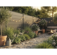 Moderner Garten mit grauem Sichtschutzzaun, Natursteinpflaster, Pflanzen in Terracotta-Töpfen, Lichterkette und brennender Feuerstelle.