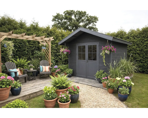 Modernes anthrazitfarbenes Gartenhaus aus Holz mit Doppeltür, Holzterrasse mit Sitzbereich, Pergola und vielen blühenden Topfpflanzen.