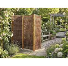 Dreiteiliger faltbarer Sichtschutz aus Weide in einem Garten mit Steinplatten, Blumen und einer Gartenbank.
