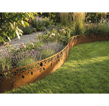 Bordure de pelouse décorative en métal aspect rouille avec motif floral séparant un massif de fleurs et une pelouse dans un jardin lumineux.