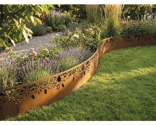 Bordure de pelouse décorative en métal aspect rouille avec motif floral séparant un massif de fleurs et une pelouse dans un jardin lumineux.