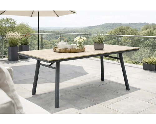 Table de jardin moderne avec plateau aspect bois et cadre en métal foncé sur une terrasse avec plantes et vue sur le paysage.