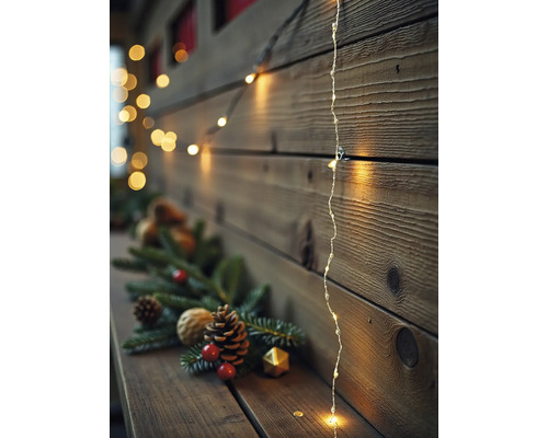 Warmweiße LED-Lichterkette an einer Holzwand mit Tannenzweigen, Tannenzapfen und roten Beeren auf einem Holzregal.