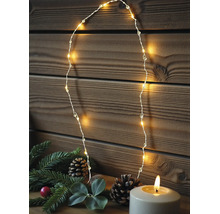 Warmweiße LED-Drahtlichterkette vor einer Holzwand, dekoriert mit Tannenzweigen, Zapfen und einer brennenden Kerze.