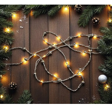 LED-Lichterkette mit Perlen auf Holzuntergrund, dekoriert mit Tannenzweigen, Zapfen und Weihnachtsschmuck in einer festlichen Anordnung.