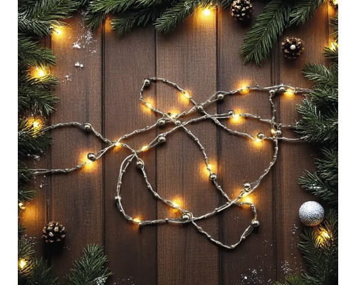 LED-Lichterkette mit Perlen auf Holzuntergrund, dekoriert mit Tannenzweigen, Zapfen und Weihnachtsschmuck in einer festlichen Anordnung.