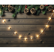 LED-Lichterkette auf Holzgrund mit Tannenzweigen und Zapfen dekoriert.