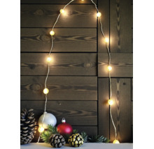 LED Lichterkette mit warmweißen Kugeln und Weihnachtsdekoration aus Tannenzapfen und Kugeln vor einer dunklen Holzwand.