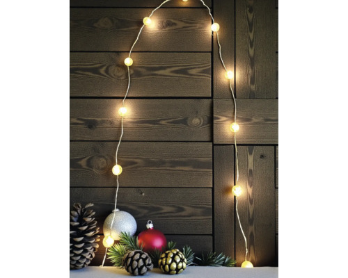 LED Lichterkette mit warmweißen Kugeln und Weihnachtsdekoration aus Tannenzapfen und Kugeln vor einer dunklen Holzwand.