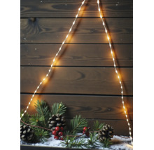 LED Lichterkette in Tannenbaumform vor einer dunklen Holzwand mit Tannenzweigen, Zapfen und roten Beeren auf Kunstschnee.