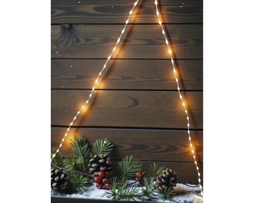 LED Lichterkette in Tannenbaumform vor einer dunklen Holzwand mit Tannenzweigen, Zapfen und roten Beeren auf Kunstschnee.