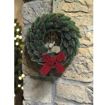 Weihnachtskranz mit Tannennadeln, roten Beeren, einer roten Schleife und einer Rehfigur an einer Steinwand.