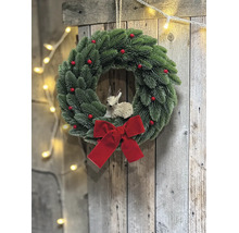 Künstlicher Adventskranz mit grünen Tannenzweigen, roten Beeren, einer großen roten Schleife und einer Rehfigur an einer Holzwand.