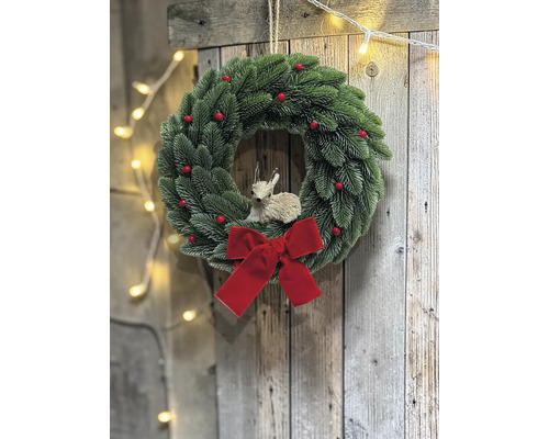 Künstlicher Adventskranz mit grünen Tannenzweigen, roten Beeren, einer großen roten Schleife und einer Rehfigur an einer Holzwand.