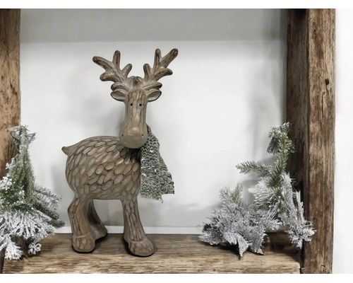 Dekorative Rentierfigur mit Schal und künstlichen Tannenbäumen auf einem Holzregal.