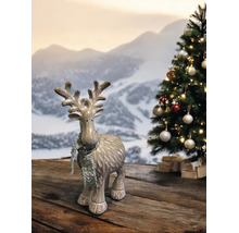 Rentier-Figur mit silbernem Glitzerschal vor einem geschmückten Weihnachtsbaum und Bergkulisse auf einem Holztisch.