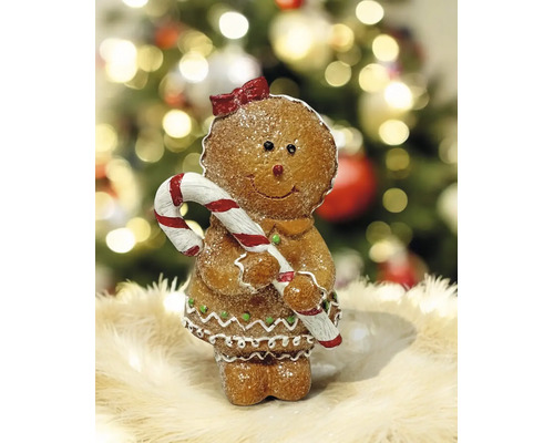Lebkuchenfigur als Mädchen mit Zuckerstange und roter Schleife, Weihnachtsdekoration vor festlichem Hintergrund.
