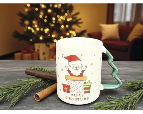 Weihnachtstasse mit Weihnachtsmann-Motiv, Geschenken und Henkel in Tannenbaumform auf einem Tisch mit Tannenzweigen und Zimtstangen.