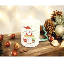 Weihnachtstasse aus Keramik mit Weihnachtsmann-Motiv und Henkel in Tannenbaumform auf Holzoberfläche mit Tannenzapfen und Nüssen.