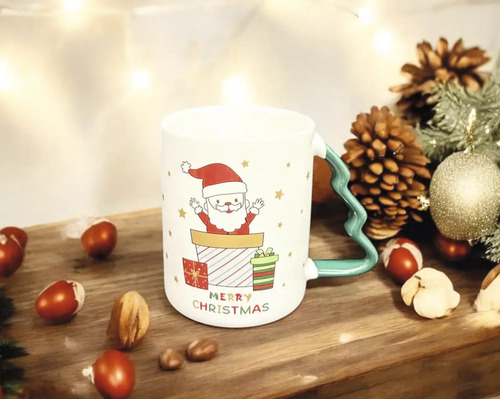 Weihnachtstasse aus Keramik mit Weihnachtsmann-Motiv und Henkel in Tannenbaumform auf Holzoberfläche mit Tannenzapfen und Nüssen.