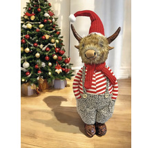 Weihnachtsdekoration Highland-Rind-Figur mit roter Weihnachtsmütze, Schal und gestreiftem Oberteil neben einem geschmückten Tannenbaum.