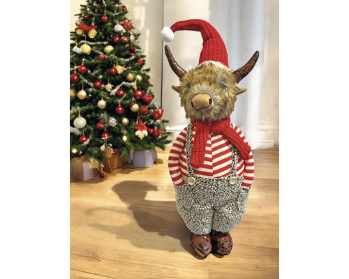 Weihnachtsdekoration Highland-Rind-Figur mit roter Weihnachtsmütze, Schal und gestreiftem Oberteil neben einem geschmückten Tannenbaum.