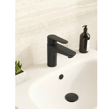 Mitigeur de lavabo moderne noir mat sur un lavabo blanc dans une salle de bains lumineuse avec distributeur de savon noir et petite plante.