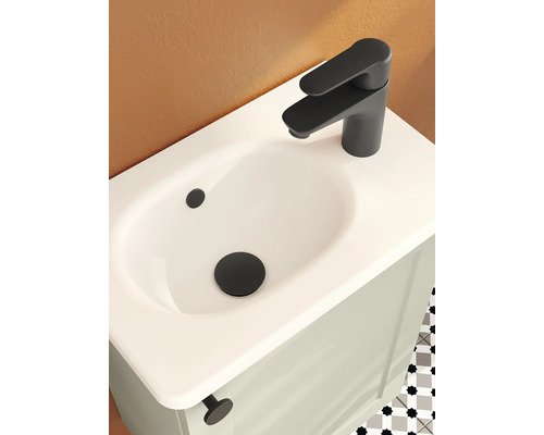 Lavabo avec mitigeur noir mat et bonde sur un meuble sous-lavabo clair dans une salle de bain moderne.