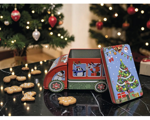 Weihnachts-Guetzlidose aus Metall in Lastwagenform mit Motiven auf einer dunklen Fläche neben Lebkuchen und einem Weihnachtsbaum.