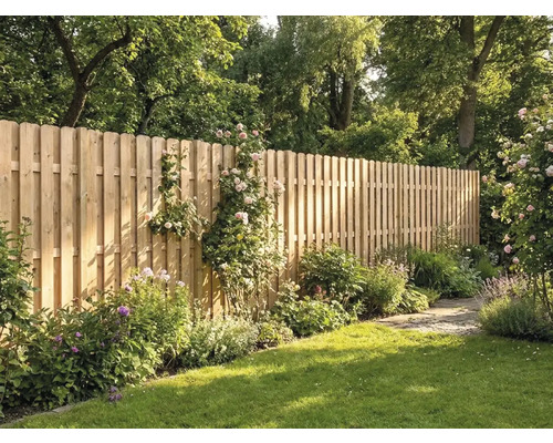 Haute clôture en bois composée de lattes verticales à têtes arrondies dans un jardin ensoleillé avec pelouse, fleurs et arbres.