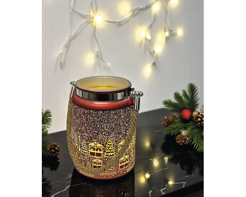 Rotes Weihnachts-LED-Windlicht mit winterlichem Dorf-Motiv, Seilgriff und Metallrand neben Tannenzweigen auf einer reflektierenden Oberfläche.