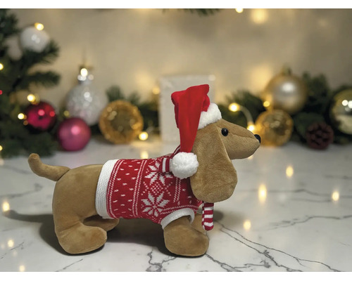 Plüschtier Dackel mit rotem Weihnachtspullover und Weihnachtsmütze vor weihnachtlicher Dekoration.