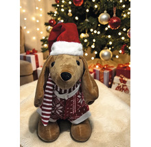 Stoffhund mit Weihnachtsmütze, gestreiftem Schal und Pullover vor einem geschmückten Weihnachtsbaum mit Geschenken.
