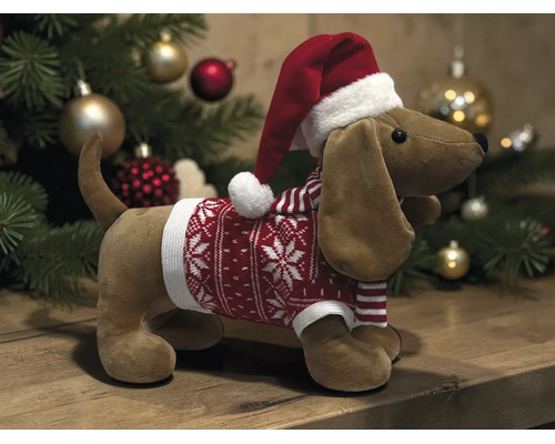 Plüsch-Dackel mit Weihnachtsmütze und rotem Weihnachtspullover vor einem Weihnachtsbaum.