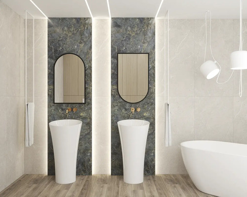 Salle de bains moderne avec deux lavabos colonnes blancs devant du marbre foncé, deux miroirs, robinetterie dorée et baignoire îlot.