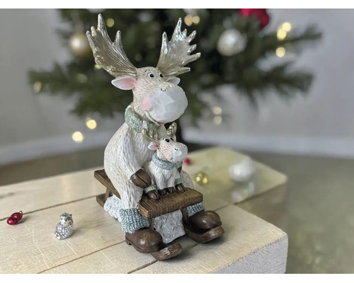Weihnachtsdekoration mit zwei Elchfiguren, groß und klein, sitzend auf einem Holzschlitten vor einem Weihnachtsbaum.