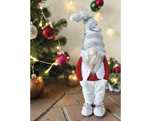 Weihnachtsgnom mit grauer Mütze, weißem Bart, rotem Oberteil und weißer Hose vor einem geschmückten Tannenbaum mit Lichtern.