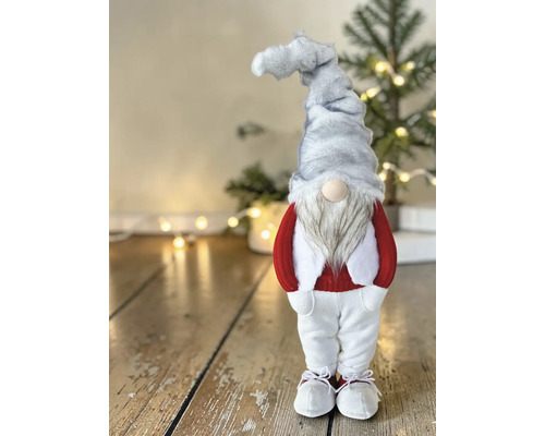 Stehende Weihnachtsfigur Wichtel mit grauer Zipfelmütze, weißem Bart, rotem Pullover und weißer Hose auf einem Holzfußboden.