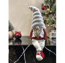 Weihnachtswichtel als Kantenhocker mit grauer Zipfelmütze, langem Bart, rotem Pullover und weißer Hose vor einer festlichen Dekoration.