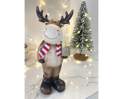 Weihnachtsdekoration Rentier-Figur mit Schal, Stiefeln und Geschenkbox vor einem kleinen Weihnachtsbaum.