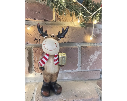 Dekorative Weihnachtsfigur Elch mit Schal und goldenem Geschenk vor einer Backsteinwand mit Beleuchtung.