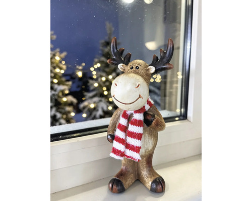 Weihnachtsfigur Elch mit rot-weiss gestreiftem Schal auf einer Fensterbank vor einem winterlichen Hintergrund.