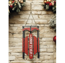 Weihnachtsdekoration aus einem Holzschlitten mit der Aufschrift Snow Flyer, hängend an einer Steinwand dekoriert mit Tannenzweigen.