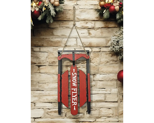 Weihnachtsdekoration aus einem Holzschlitten mit der Aufschrift Snow Flyer, hängend an einer Steinwand dekoriert mit Tannenzweigen.