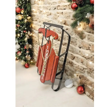 Dekorativer roter Schlitten aus Holz und schwarzem Metall mit Schriftzug SNOW, rustikale Weihnachtsdekoration vor einer Backsteinwand mit Tannenbaum.
