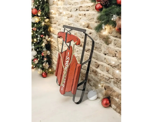 Dekorativer roter Schlitten aus Holz und schwarzem Metall mit Schriftzug SNOW, rustikale Weihnachtsdekoration vor einer Backsteinwand mit Tannenbaum.